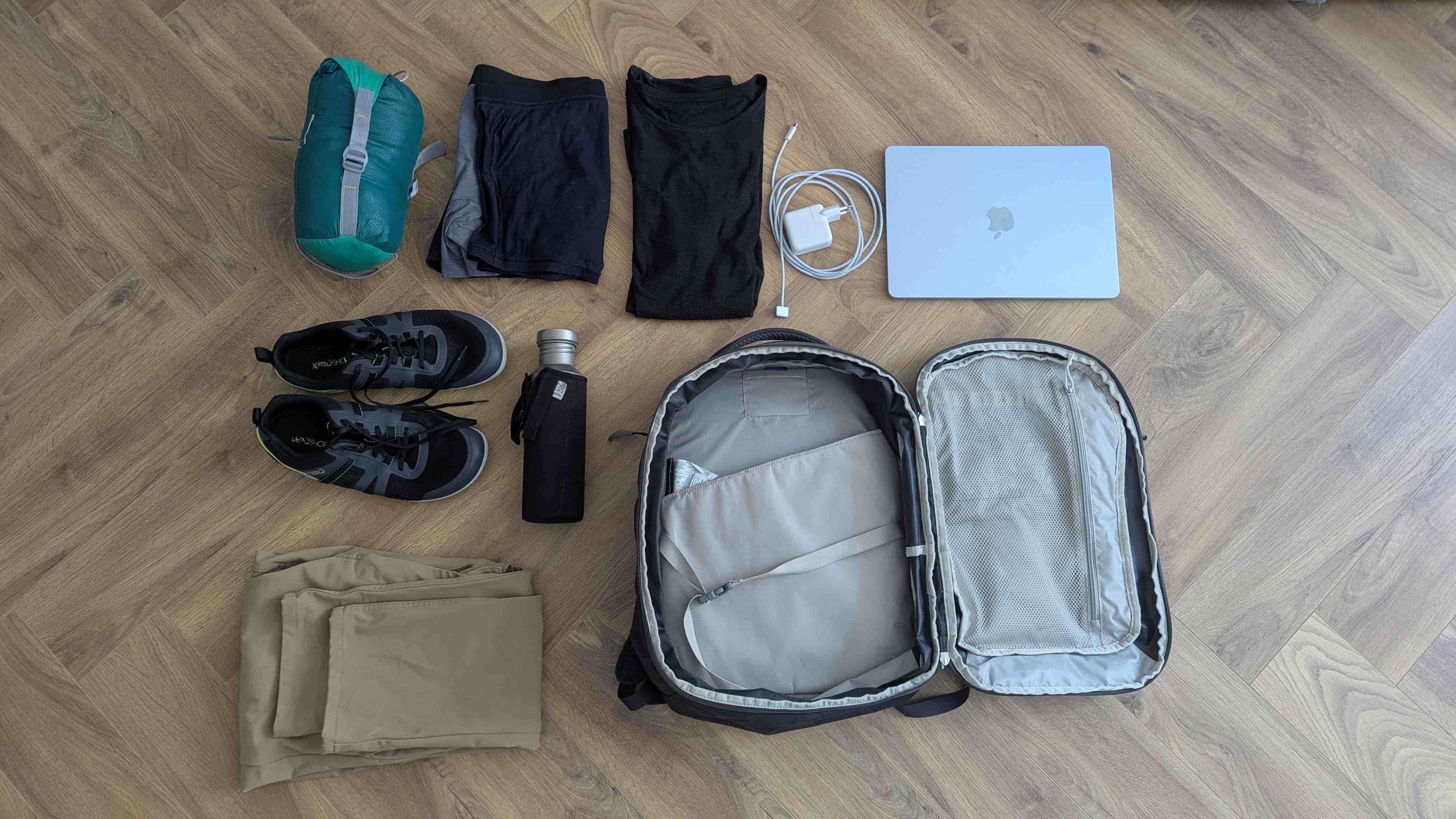 Top-down view of the Osprey Daylite 26+6L backpack open with all its contents laid out: MacBook, shoes, sleeping bag, clothes, and water bottle